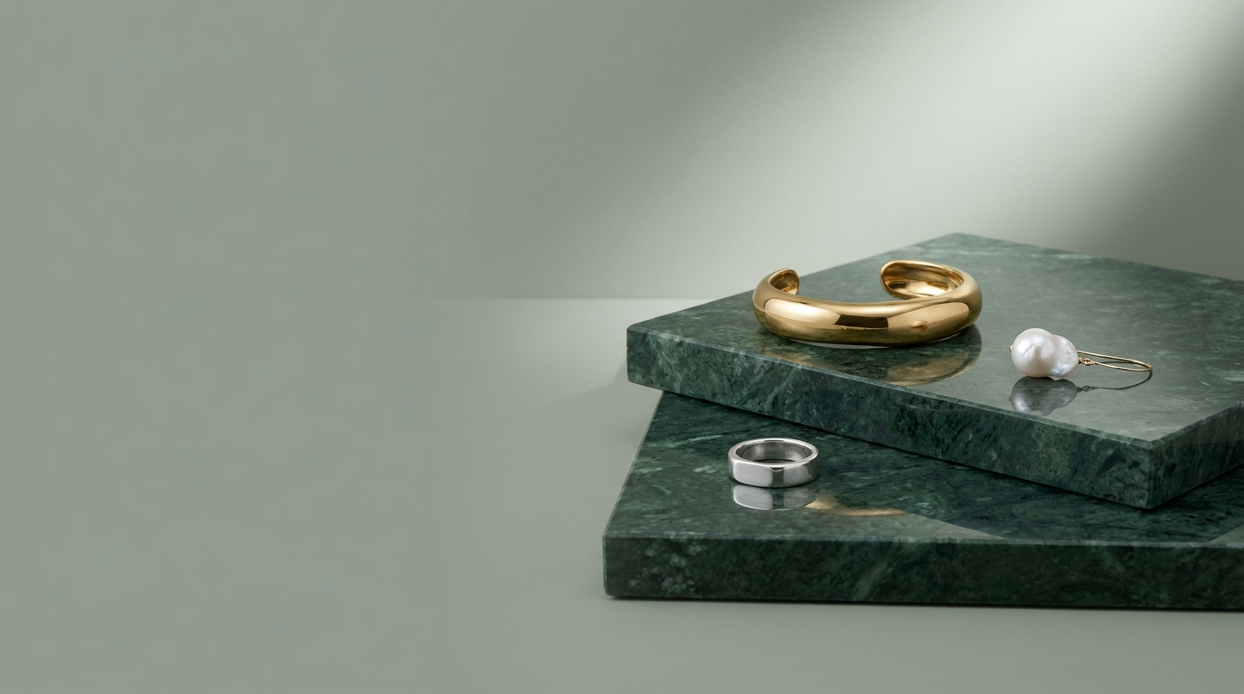 Gold cuff, pearl earring and silver ring on polished green marble, modern studio light