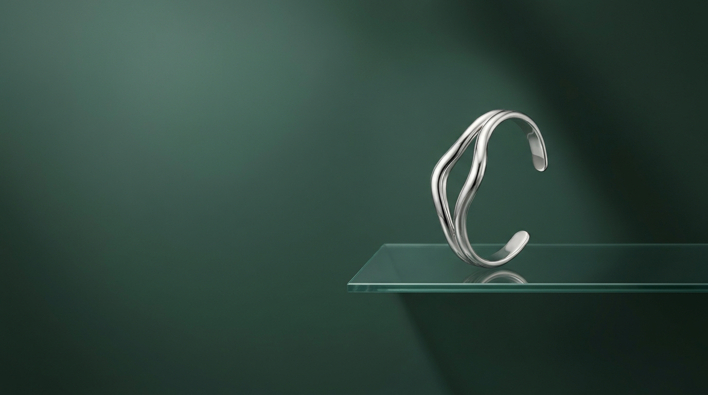 Silver torque bangle on a glass shelf against a deep verdigris studio backdrop